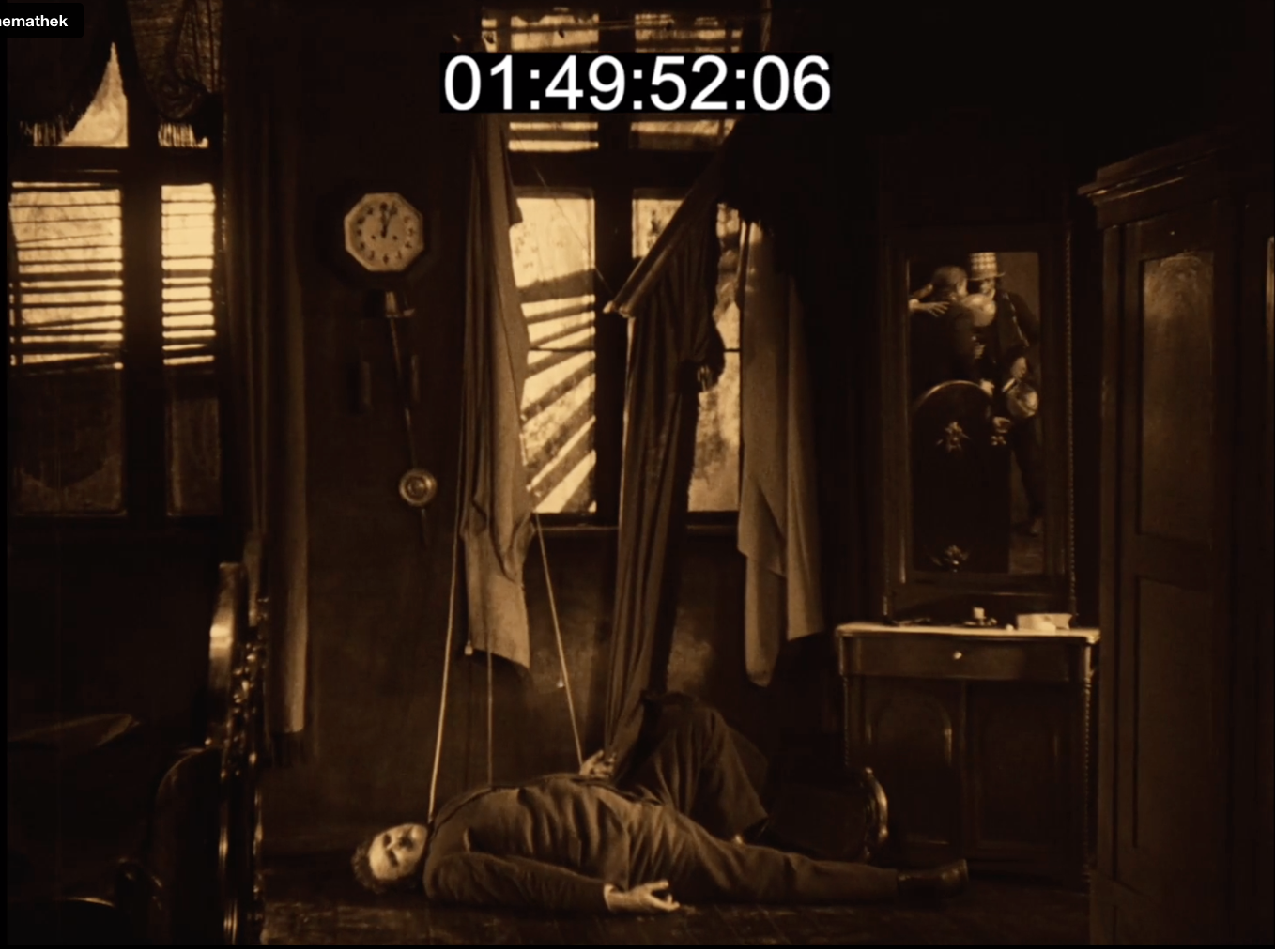 Film still from Sylvester: a body lies on the floor beneath a wall clock, reflected in a mirror behind.