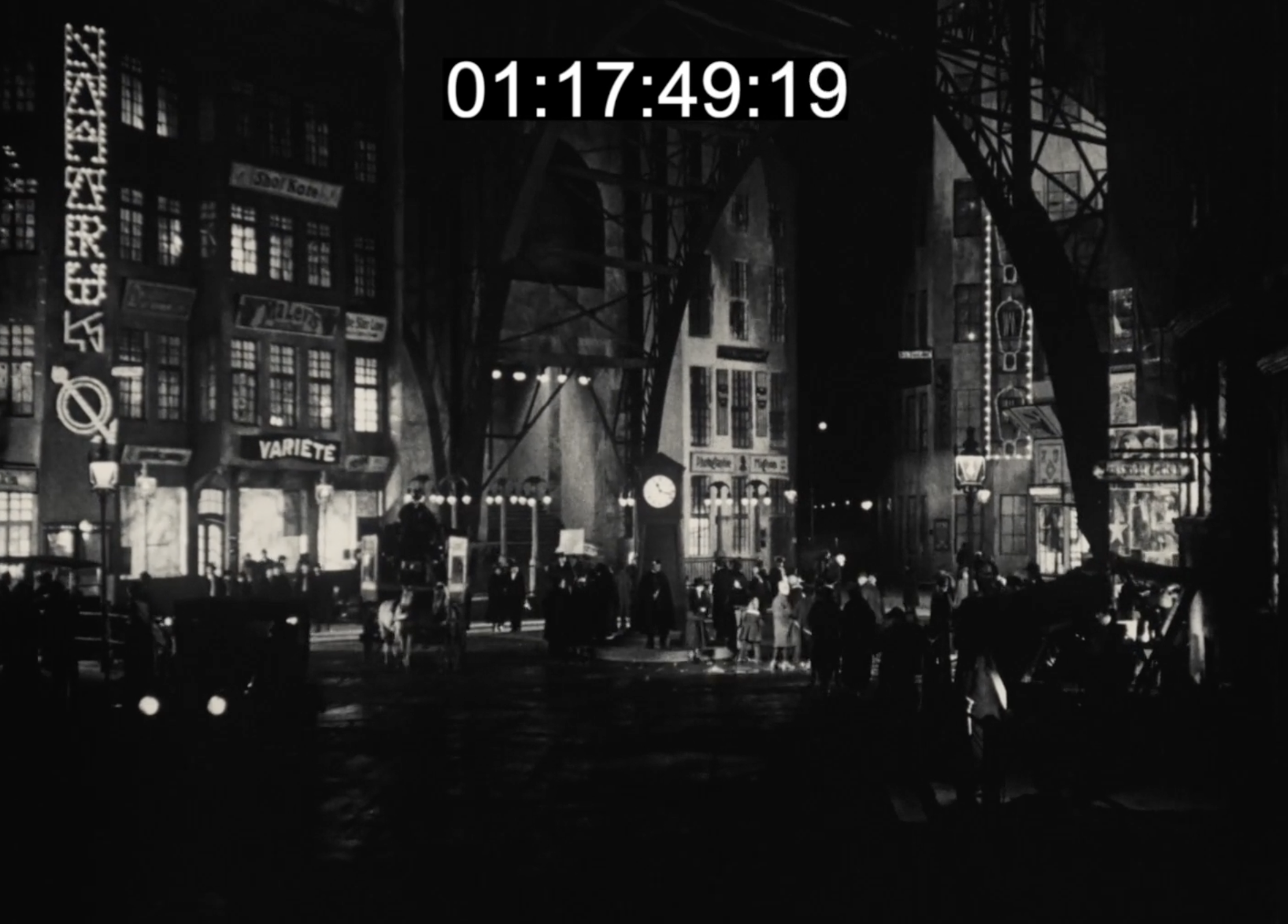 Film still from Sylvester: a bustling, illuminated night street with a crowd gathered around a clock, cabaret signage overhead.