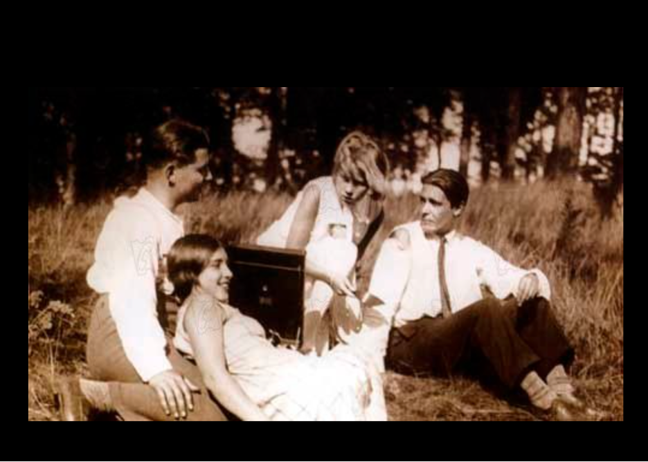 Film still from Menschen am Sonntag (People on Sunday): four young people relax in a sunny meadow around a portable gramophone.