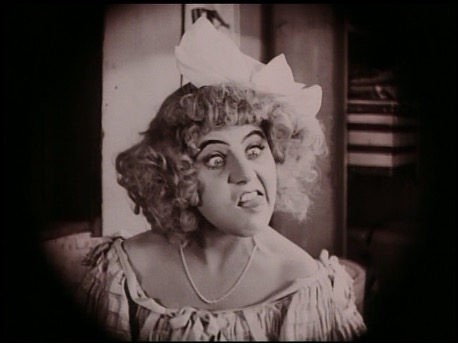 Film still: Ossi Oswalda pulls an exaggerated grimace, tongue out, in a face-making close-up.