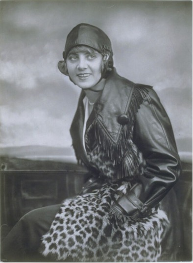 Portrait of a woman in a fringed leather jacket and leopard-print skirt, wearing a cloche hat.