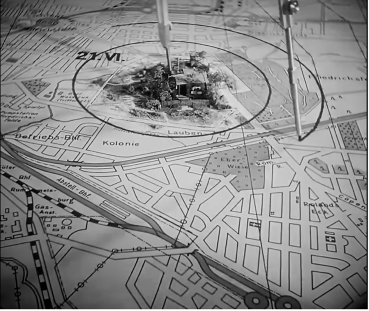 Film still from M: an angled view of the compass's circle centered on the miniature garden house, its shadow rippling over the model's roof.